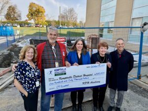 People standing with construction going on in the background, handing over a cheque to the hospital.